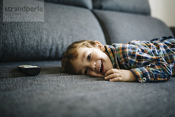 Porträt des lächelnden kleinen Jungen auf der Couch neben der Fernbedienung