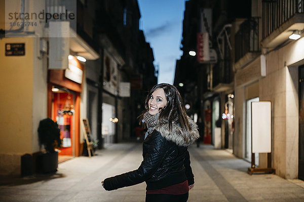 Spanien  Reus  Porträt einer lächelnden jungen Frau  die abends in der Fußgängerzone spazieren geht.