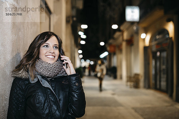 Spanien  Reus  Porträt einer lächelnden jungen Frau beim Telefonieren mit dem Smartphone bei Nacht