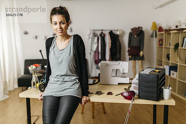 Junge Modedesignerin in ihrem Atelier  an den Schreibtisch gelehnt