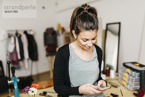 Junge Modedesignerin  die in ihrem Atelier mit dem Smartphone arbeitet.