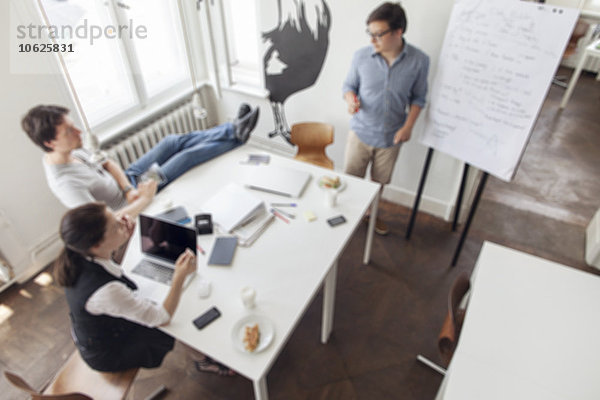 Verschwommener Blick auf drei kreative Geschäftsleute bei einem Meeting in einem modernen Büro