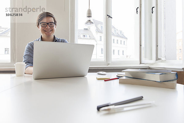 Lächelnder junger Geschäftsmann mit Laptop in einem modernen Büro