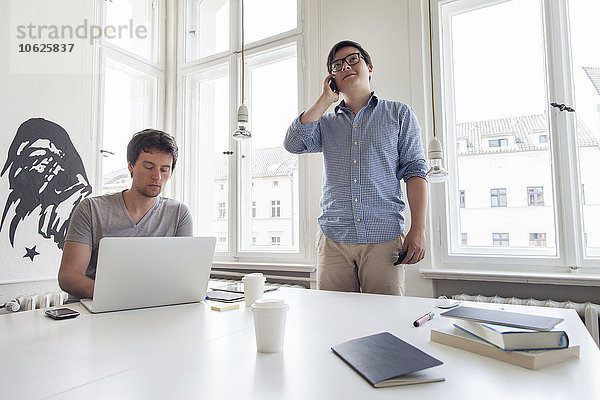 Zwei kreative Geschäftsleute mit Laptop und Handy in einem modernen Büro