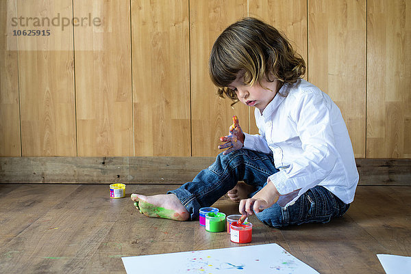 Kleiner Junge auf Holzboden sitzend mit Fingerfarben