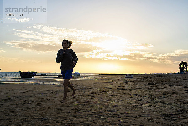Spanien  Puerto Real  Frau beim Joggen am Strand bei Sonnenuntergang