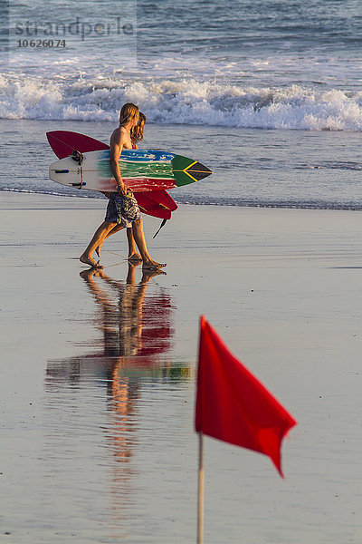 Indonesien  Bali  zwei Surfer  die mit ihren Boards am Strand entlanglaufen.