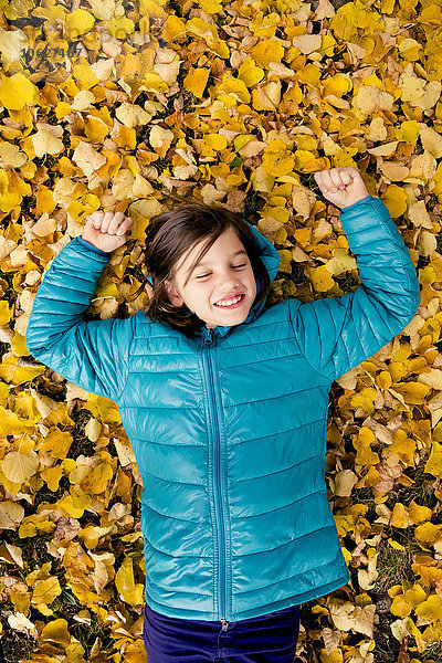 Lächelndes Mädchen auf dem mit Herbstblättern bedeckten Boden liegend