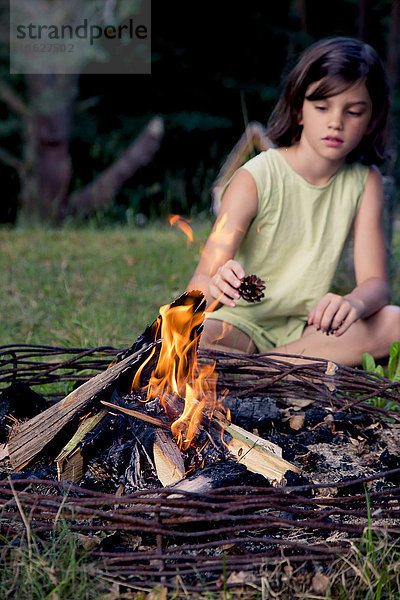 Mädchen sitzend auf einer Wiese hinter einem Lagerfeuer