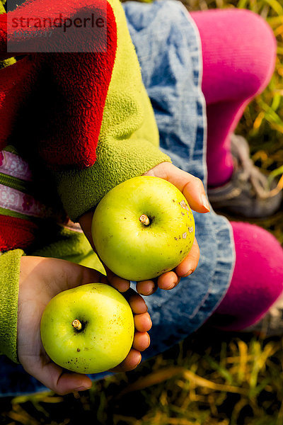 Kleines Mädchen mit zwei grünen Äpfeln  Nahaufnahme