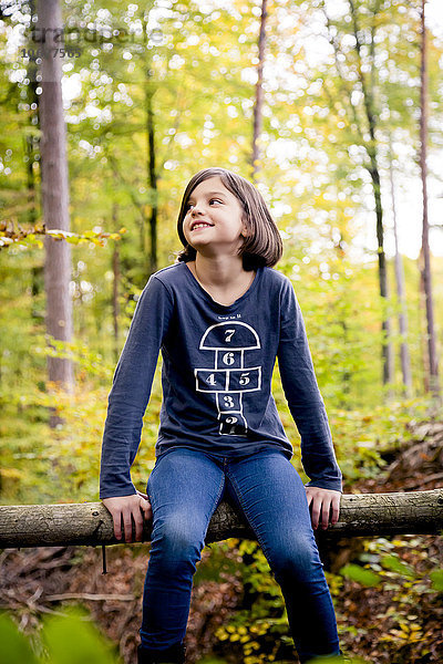 Porträt eines glücklichen Mädchens  das auf einer Stange im Wald sitzt.