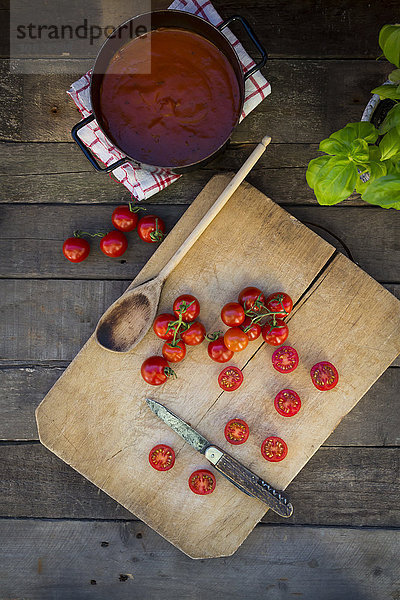 Scheiben und ganze Tomaten auf Hackbrett und Topf mit Tomatensuppe