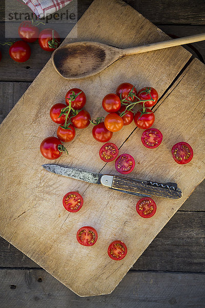 Scheiben und ganze Tomaten  Kochlöffel und Messer auf Schneidbrett