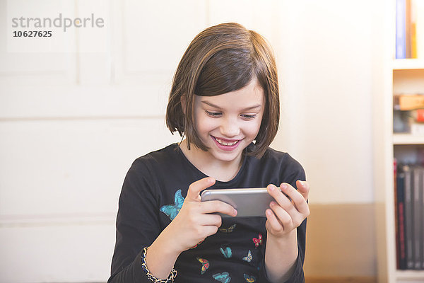 Porträt eines lächelnden Mädchens beim Anblick des Smartphones