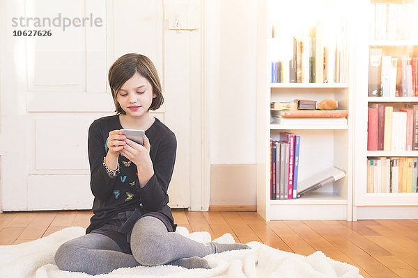Porträt eines Mädchens  das mit dem Smartphone auf der Decke auf dem Boden sitzt.