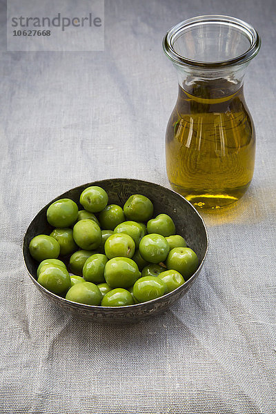 Schale mit grünen Oliven und Karaffe mit Olivenöl
