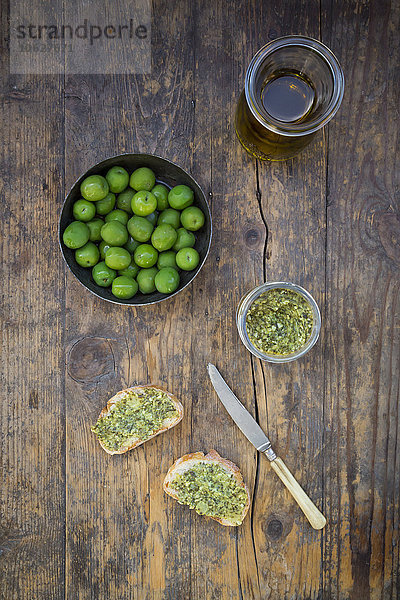 Schale mit grünen Oliven  Karaffe mit Olivenöl  Messer und Brotscheiben mit Olivenaufstrich
