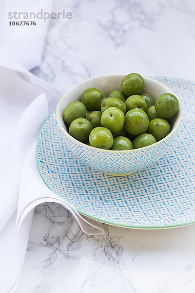 Schale mit grünen Oliven auf Teller und weißem Marmor