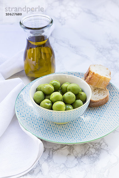 Schale mit grünen Oliven  Brotscheiben und Karaffe mit Olivenöl