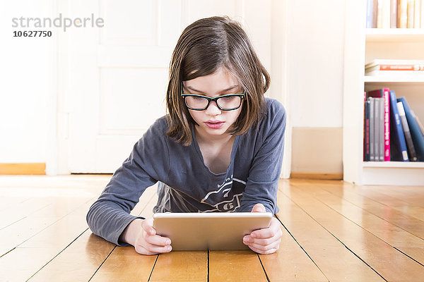 Porträt eines Mädchens auf Holzboden liegend mit digitalem Tablett