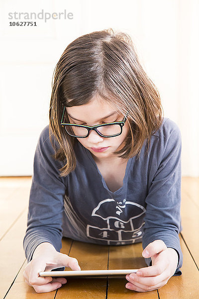Porträt eines Mädchens auf Holzboden liegend mit digitalem Tablett