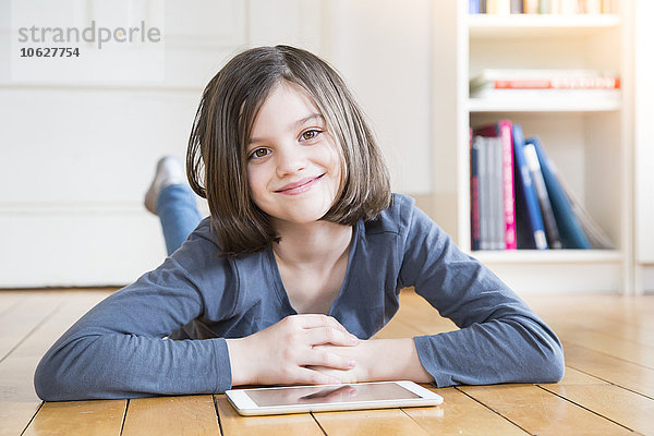 Porträt eines lächelnden Mädchens auf Holzboden liegend mit digitalem Tablett