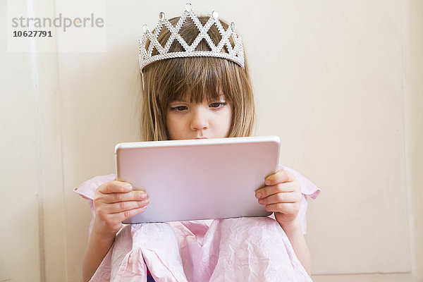 Kleines Mädchen verkleidet als Prinzessin beim Betrachten des digitalen Tabletts