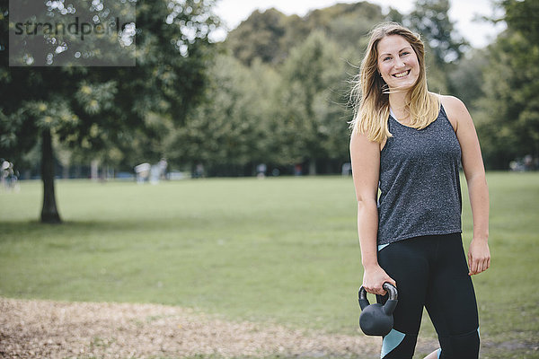 Lächelnde junge Frau mit Kesselglocke im Park