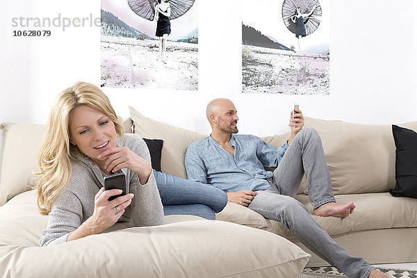 Reife Paare  die auf dem Sofa sitzen und ihre Smartphones benutzen.