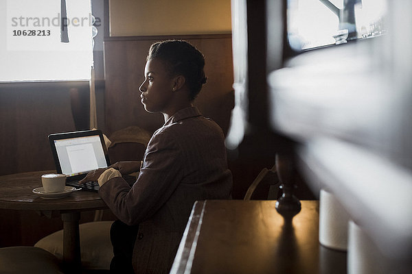 Junge Frau sitzt in einem Café und arbeitet mit einem Laptop.