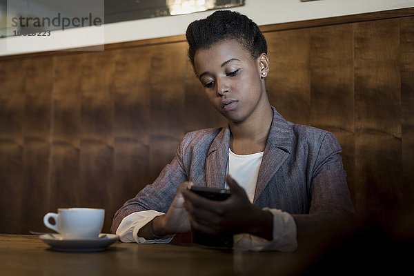 Portrait einer jungen Frau  die mit dem Smartphone in einem Café sitzt.