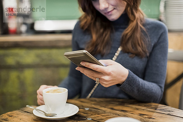 Frau überprüft ihr Smartphone in einem Cafe