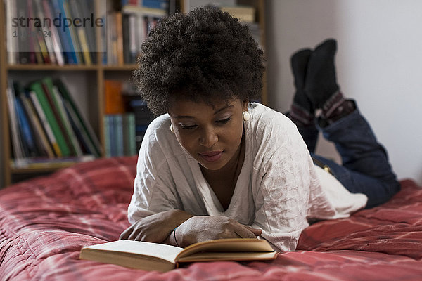 Junge Frau  die zu Hause auf ihrem Bett liegt und ein Buch liest.