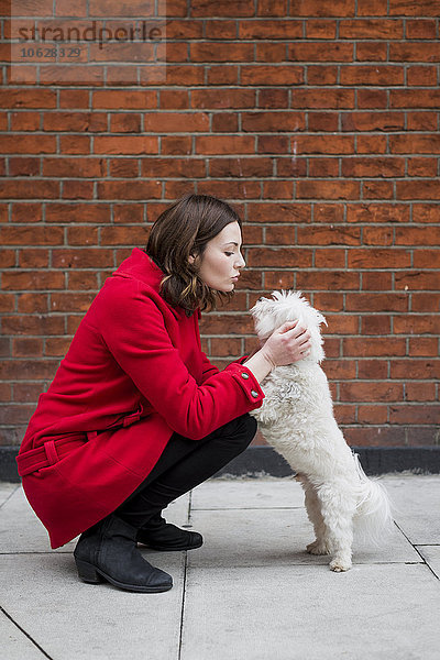 UK  London  junge Frau kauert auf dem Bürgersteig  von Angesicht zu Angesicht zu ihrem Hund.
