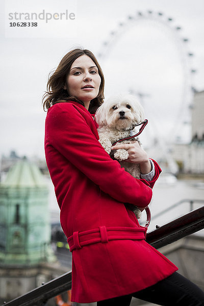 UK  London  Porträt einer jungen Frau mit Hund auf den Armen und London Eye im Hintergrund