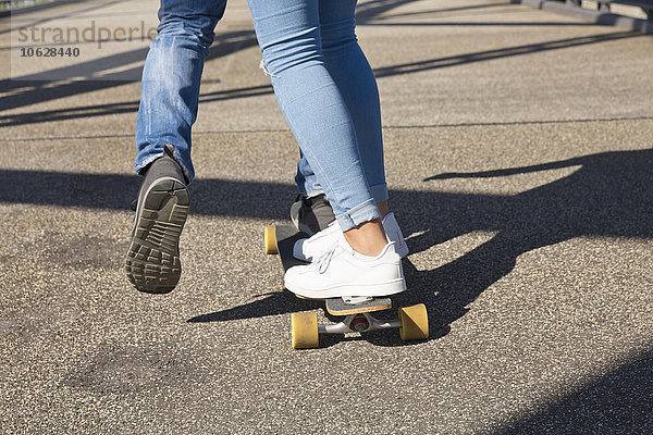Beine eines jungen Paares beim Fahren auf einem Skateboard