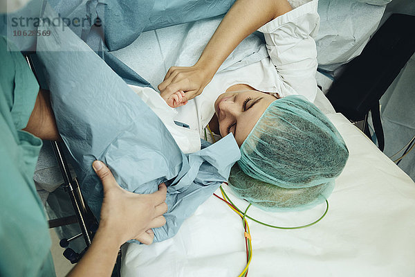 Mutter berührt ihr Neugeborenes direkt nach dem Kaiserschnitt.