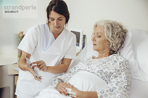 Krankenschwester erklärt ältere Frau im Krankenhaus digitale Tablette
