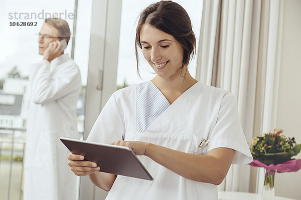 Krankenschwester mit digitalem Tablett im Krankenhauszimmer  Arzt ruft im Hintergrund an