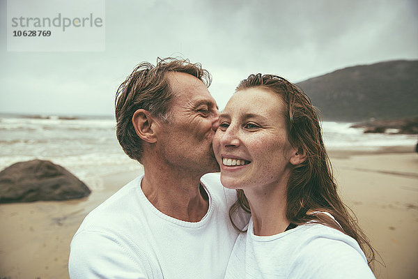 Brasilien  Florianopolis  Mann küsst Frau am Strand an einem regnerischen Tag