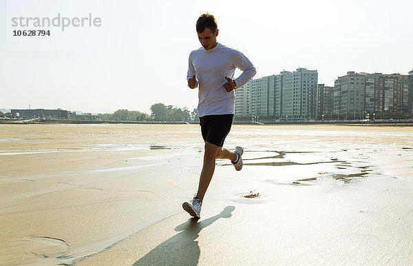 Spanien  Asturien  Gijon  junger Mann  der am Strand rennt.