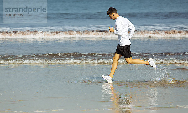 Spanien  Asturien  Gijon  junger Mann  der am Strand rennt.