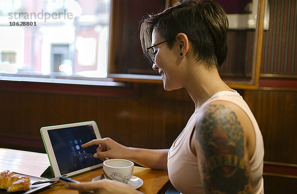 Tätowierte junge Frau sitzend in einem Coffee-Shop mit digitaler Tablette