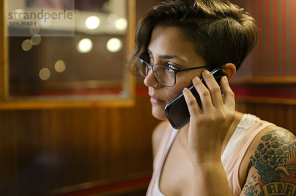 Tätowierte junge Frau sitzt in einem Café und redet am Telefon