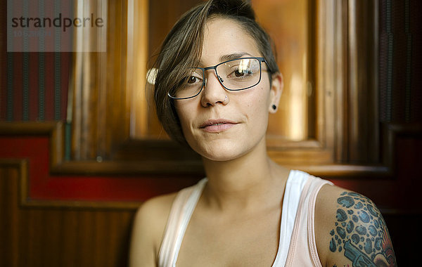 Portrait einer tätowierten jungen Frau mit Brille