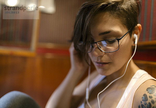 Tätowierte junge Frau beim Musikhören mit Kopfhörern