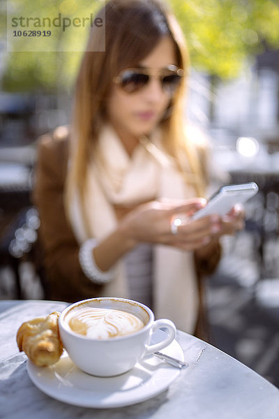 Spanien  Gijon  Cup of cappucino  junge Frau im Hintergrund mit Smartphone