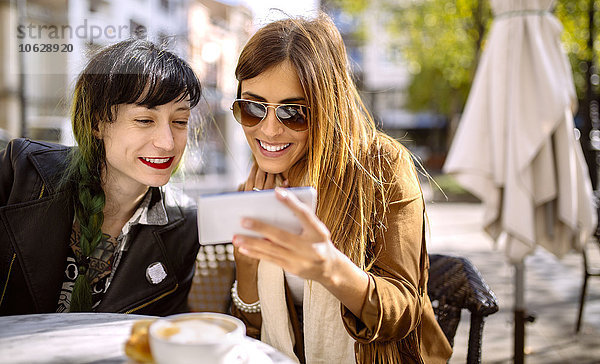 Spanien  Gijon  Zwei Freunde im Cafe beim Blick auf Smartphone