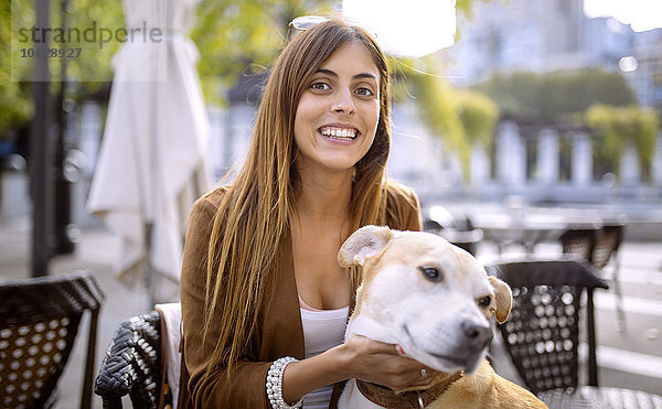 Spanien  Gijon  Junge Frau sitzt im Straßencafé  kitzelt ihren Hund