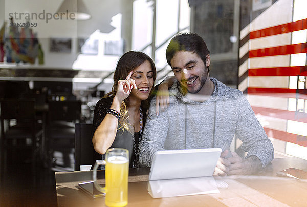 Glückliches junges Paar mit digitalem Tablett in einer Kneipe